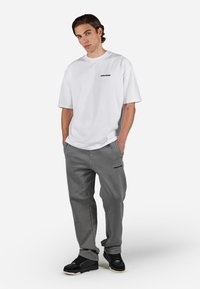 Tricou alb oversized cu logo negru, asortat cu pantaloni de trening gri ce au un logo similar. Sneakersi negri completează ținuta.