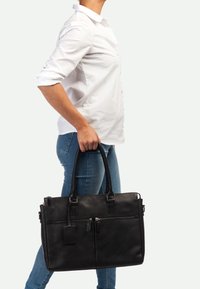 Bolsa de cuero negra para portátil con dos asas superiores, bolsillos frontales con cremallera, textura suave y un sutil detalle de marca.