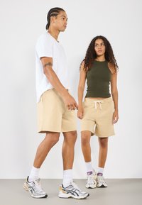Deux mannequins portant des vêtements décontractés : un t-shirt blanc à manches courtes et un short beige, associés à des baskets à motif multicolore.