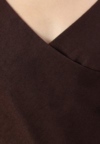 Tissu marron avec une texture lisse, présenté avec un design en V. Le matériau semble doux et léger avec un éclat subtil.