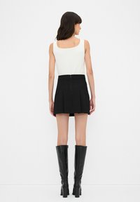 Jupe mini plissée noire avec fermeture éclair, portée avec un haut sans manches blanc et des bottes noires jusqu'aux genoux. Texture de tissu lisse.
