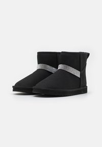 Botas negras hasta el tobillo hechas de suave gamuza, con una correa de purpurina plateada alrededor de la parte media y una suela de goma negra texturizada.