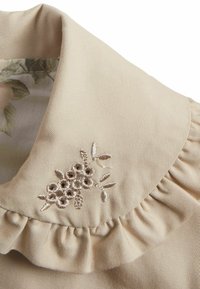 Beige stoffen kraag met een gerimpelde rand bevat bloemstickers in lichtbruine tinten. De binnenste kraag heeft een subtiel bloemmotief.