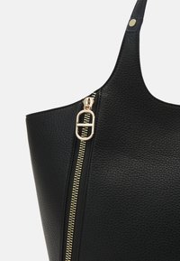 Zwarte ge textured leren tote bag met een gouden rits en hardware-accenten. Het ontwerp heeft een enkele strap en een slanke vorm.