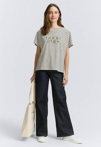Striped t-shirt in cream and black with the text "GOOD TIMES" in green, paired with wide-leg dark denim jeans and white sneakers.