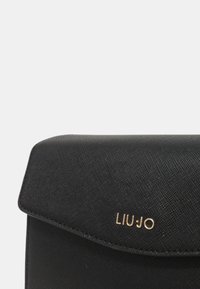 Czarna torebka syntetyczna z klapką. Posiada teksturowaną powierzchnię oraz złote logo "LIU JO" z przodu, co zapewnia elegancki design.