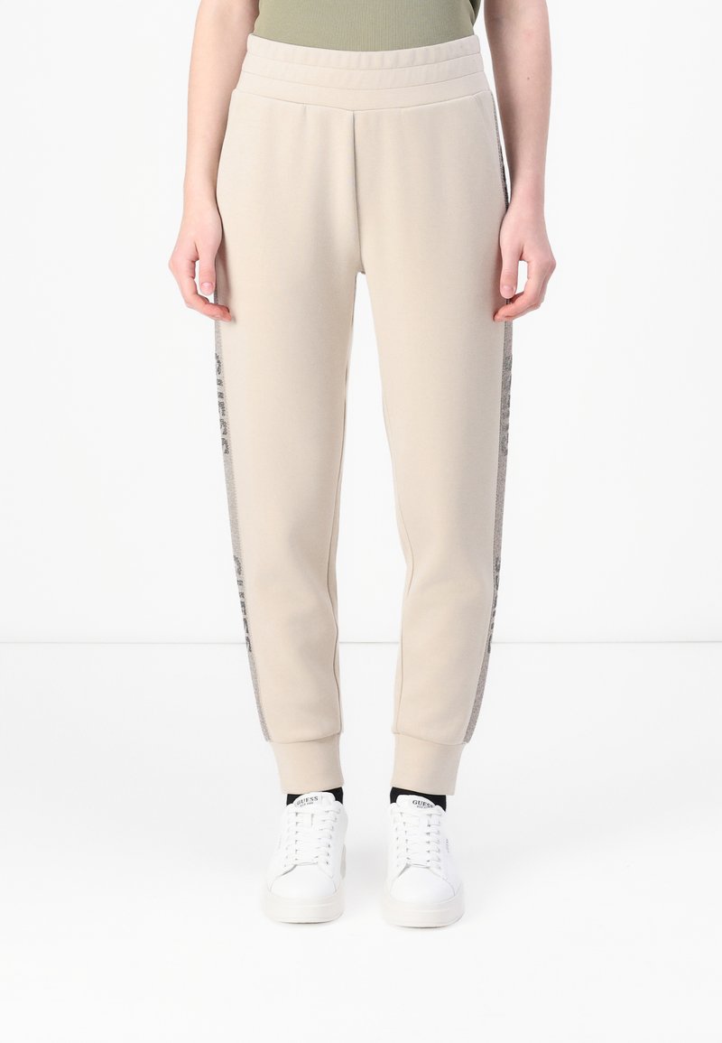 Lichtbeige sweatpants met een ribgebreide tailleband, taps toelopende enkels en zijpanelen met een subtiel patroon. Gecombineerd met witte sneakers.