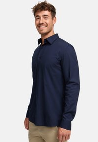 Camisa de botones de manga larga azul marino hecha de algodón, con un cuello clásico y una textura sutil. Cierre de botones y corte recto.