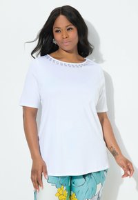  camiseta blanca de manga corta con un cuello redondo y detalles decorativos. El material parece suave y liviano.