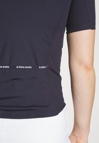 Camiseta atlética de manga corta en un azul marino oscuro con textura acanalada, que presenta un logo blanco de "BJÖRN BORG" a lo largo del dobladillo y las costuras.