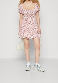 Vit blommig klänning med korta ärmar och smockad bodice. Matchad med vit väska och grå sneakers. Slät tyg, vid kjol.