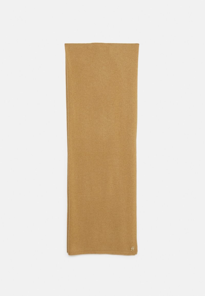 Écharpe rectangulaire couleur chameau doux, pliée dans le sens de la longueur, avec un petit logo brodé près d'un des coins.