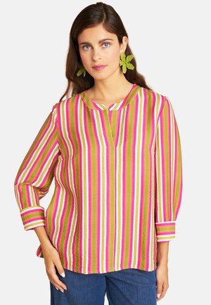 Woman wearing a pink, green, and white vertical striped blouse with 3/4 sleeves and green leaf-shaped earrings.