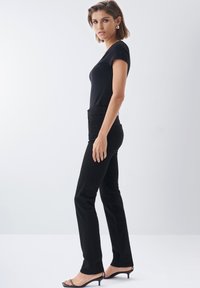 Camiseta negra ajustada de manga corta combinada con jeans negros de cintura alta. Los accesorios incluyen grandes pendientes de oro y tacones negros.