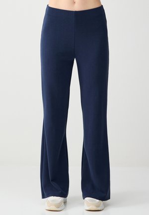 Granatowe, prążkowane spodnie o szerokich nogawkach noszone z białymi trampkami, odsłaniające brzuch i dolne partie nóg na jasnym, jednolitym tle.