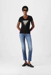 T-shirt nera con scollo a V e logo triangolare metallico, abbellita con strass, abbinata a jeans blu chiaro a gamba dritta e mocassini neri.