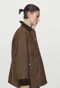 Braune, übergroße Jacke mit einem Cordkragen, Seitentaschen und gerippten Bündchen. Über einem cremefarbenen, gerippten Pullover getragen.