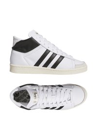 Sneaker alte bianche con dettagli in pelle nera e tre strisce nere. Suola in gomma testurizzata e logo Adidas dorato sulla linguetta.