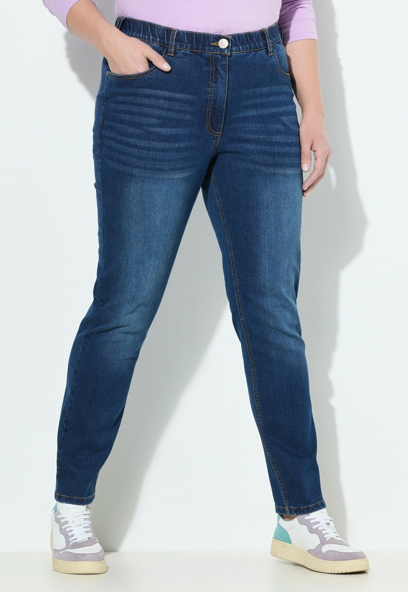 Jeans de mezclilla de corte ajustado, lavado oscuro, con cinturilla elástica, bolsillos frontales y costuras decorativas a lo largo de la pierna.