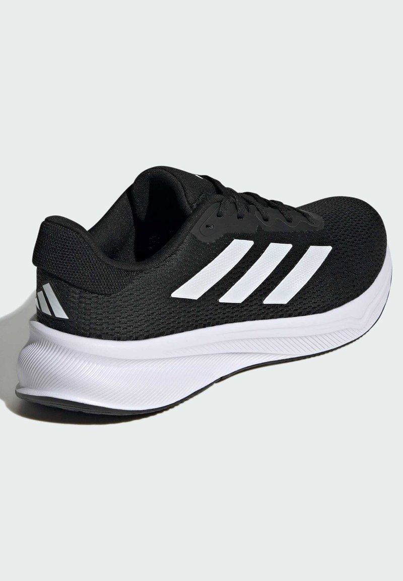 Zapatilla deportiva negra con una parte superior texturizada, rayas blancas y una suela blanca acolchada con detalles estriados.