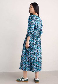 Blumendruckkleid mit Smock-Taille, Dreiviertelärmeln und fließender Silhouette in Blau-, Grün- und Lilatönen.