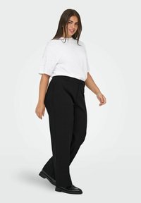 Pantaloni neri su misura con gamba dritta, indossati con una t-shirt bianca di taglio largo. La t-shirt presenta decorazioni sulle maniche.