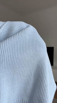 Tessuto lavorato a maglia azzurro chiaro con una trama a coste, che pende lungo il bordo. Morbido e di peso medio con dettagli di cucitura visibili.