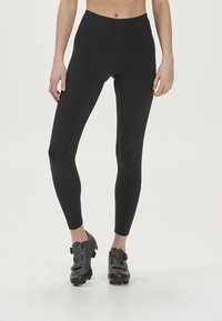 Czarne legginsy sportowe z wysokim stanem i dopasowanym krojem, wykonane z gładkiego, elastycznego materiału. W zestawie czarne buty rowerowe z klamrami.