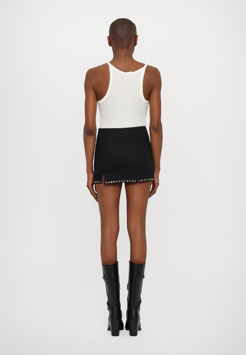 Sort mini nederdel med udskæringer og sølvnitter, parret med en hvid tanktop og båret med knæhøje sorte støvler.