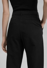Pantalon noir taille haute en tissu doux, avec une finition lisse, deux poches arrière et une coupe ajustée.