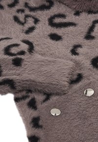 Luddig grå tröja med svart leopardtryck, med en strukturerad yta och silverknappar som accent. Nära bild av ärm och detaljer.