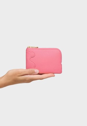 Mano sosteniendo una pequeña cartera texturizada rosa con diseño de contorno de oso y cremallera dorada sobre un fondo liso y claro.