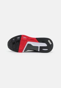 Semelle de sneaker noire et rouge avec caoutchouc texturé, motifs striés et accents blancs ; présente des éléments de traction variés et une rainure de flexion.
