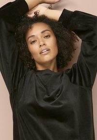 Sudadera negra de terciopelo con manga larga, corte relajado y escote pronunciado. Textura suave y detalles mínimos en la tela.