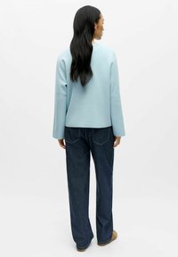 Jasnoniebieska bluzka z długim rękawem z miękkiego materiału, w połączeniu z ciemnoniebieskimi spodniami typu wide-leg. Prosty krój o luźnym fasonie z minimalnymi detalami.