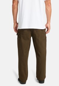 Bruine cargobroek gemaakt van duurzame stof, met zijzakken en een relaxte pasvorm, gecombineerd met een effen wit T-shirt.