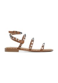 Sandali piatti beige con più cinturini decorati da borchie a forma di piramide in argento. Cinturino alla caviglia regolabile e dettagli decorativi bianchi lungo la suola.