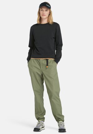 Felpa nera, pantaloni verdi e scarponi da trekking grigi. Caratteristiche includono un collo rotondo, una vita elastica e un cordino regolabile.