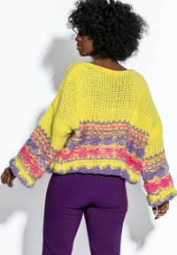 Sweter dzianinowy w jasnym żółtym kolorze, z wielokolorowymi wzorami w różowym, fioletowym i niebieskim. Luźny krój z szerokimi rękawami i ściągaczem u dołu.