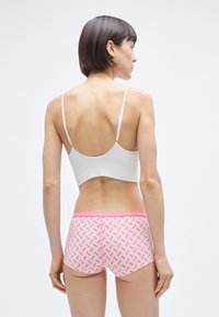 Λευκό ριμπ σουτιέν και ροζ σορτς τύπου boyshorts με ελαστική μέση. Τα σορτς έχουν γεωμετρικό σχέδιο σε διάφορες αποχρώσεις του ροζ.