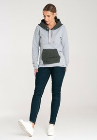 Szary hoodie z ciemnoszarym kapturem i kieszenią z przodu, z sznurkami, w połączeniu z ciemnoniebieskimi dżinsami i białymi trampkami.