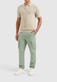 Beige gebreide poloshirt met een textuurpatroon, gecombineerd met mintgroene cargobroek met zijzakken en witte sneakers.