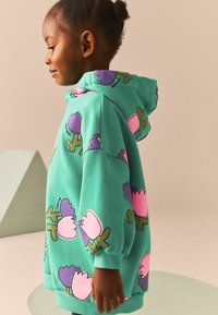 Hanorac verde cu motive florale mari în nuanțe de roz și mov. Materialul pare moale, cu o croială lejeră și glugă cu șnur.