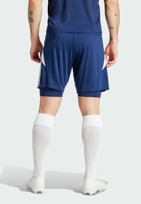 Shorts de sport marine avec des accents latéraux blancs, associés à des chaussettes blanches hauteur genou et des chaussures de football blanches, mettant en valeur un design élégant.