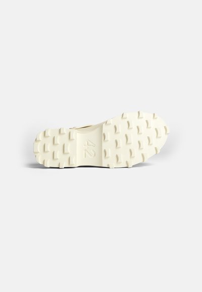 Zool van een schoen, gestructureerd rubber met uitgesproken noppen, voornamelijk off-white van kleur, met in het midden een gevormd nummer "42".