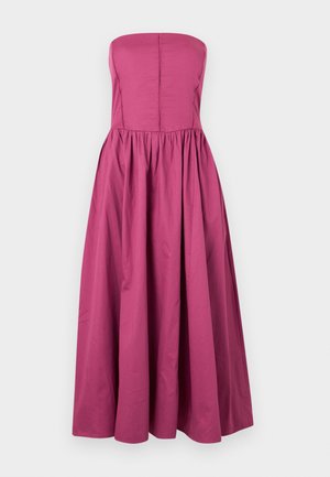 Φούξια αμάνικο φόρεμα με εφαρμοστή μπούστο, κάθετες ραφές και φουσκωτή φούστα που φτάνει μέχρι τη μέση της γάμπας σε μονόχρωμο φόντο.