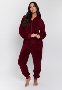 Pijama de forro polar burdeos con cierre completo, capucha y puños elásticos. Superficie texturizada, corte holgado y diseño con bolsillos laterales.