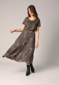 T-shirt graphique vert olive avec impression "Rock n' Rodeo", associé à une jupe longue plissée à imprimé animal et des bottines noires.