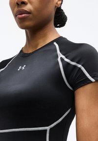 Κοντινό πλάνο του άνω μέρους του κορμού μιας γυναίκας που φοράει μαύρο αθλητικό μπλουζάκι Under Armour με λευκές ραφές και λογότυπο στο στήθος.