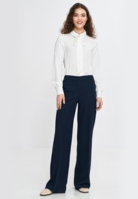 Biała bluzka z długim rękawem z detalem krawata, zestawiona z granatowymi spodniami o szerokich nogawkach, z dopasowanym krojem i subtelną teksturą.